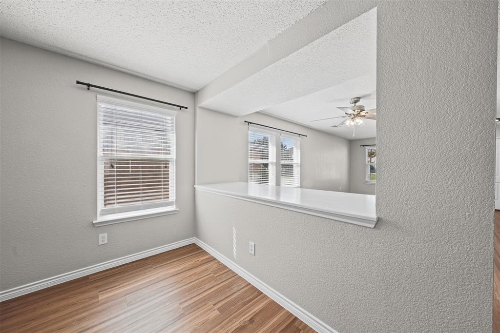 Wood-finish flooring, neutral textured walls, white-capped pass-through ledge, and windows with horizontal blinds Wood-finish flooring, neutral textured walls, white-capped pass-through ledge, and windows with horizontal blinds