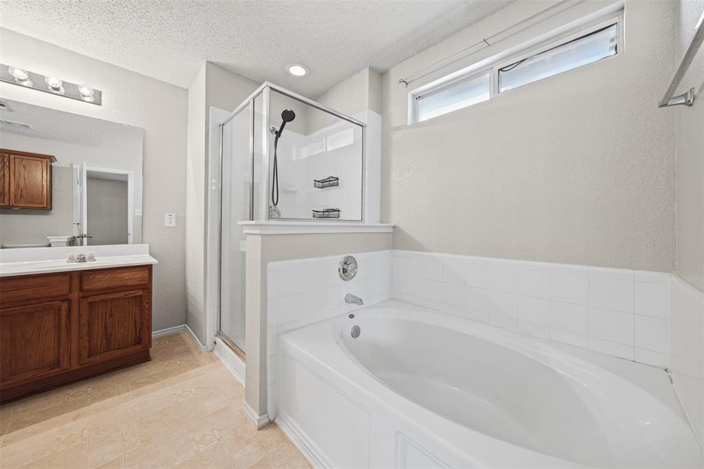 Bathroom featuring a wood-toned vanity with a white countertop, oval soaking tub with white tile surround, separate glass-enclosed shower, and clerestory window