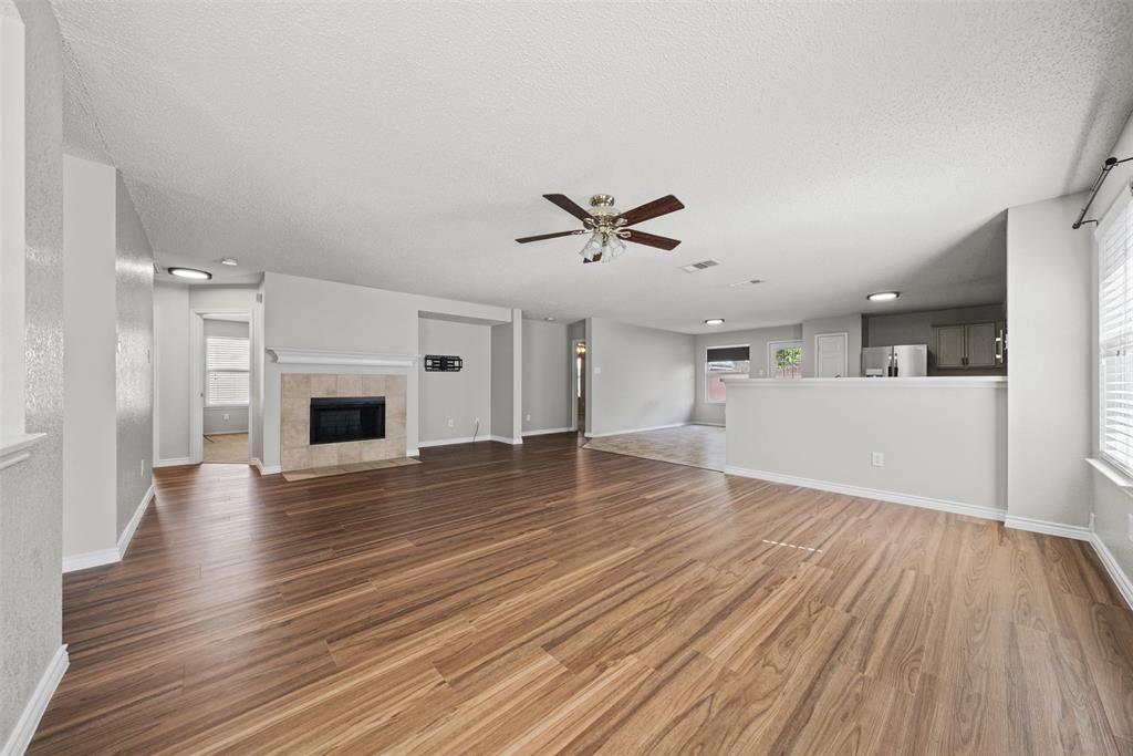 Open interior featuring wood-finish flooring, a tile-surround fireplace, a ceiling fan with integrated lighting, and a kitchen pass-through counter