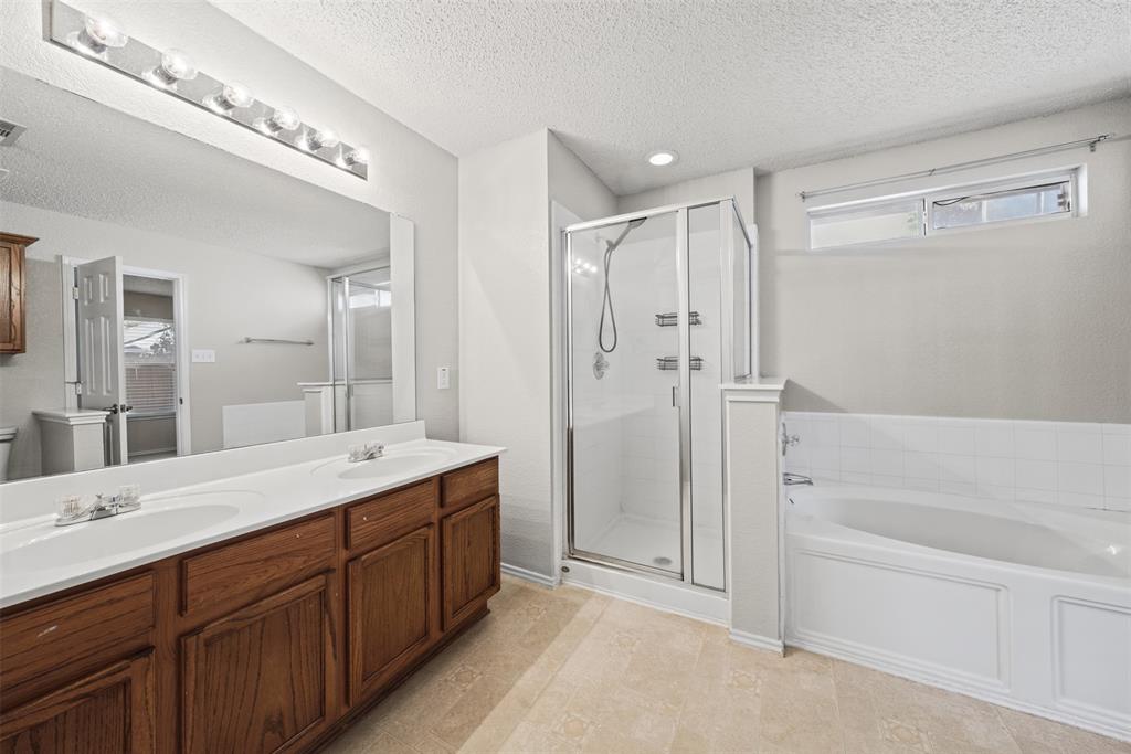 Bathroom featuring a wood-finish double vanity with dual undermount sinks, a large wall-mounted mirror, a separate glass-enclosed shower, and a soaking tub with tiled surround