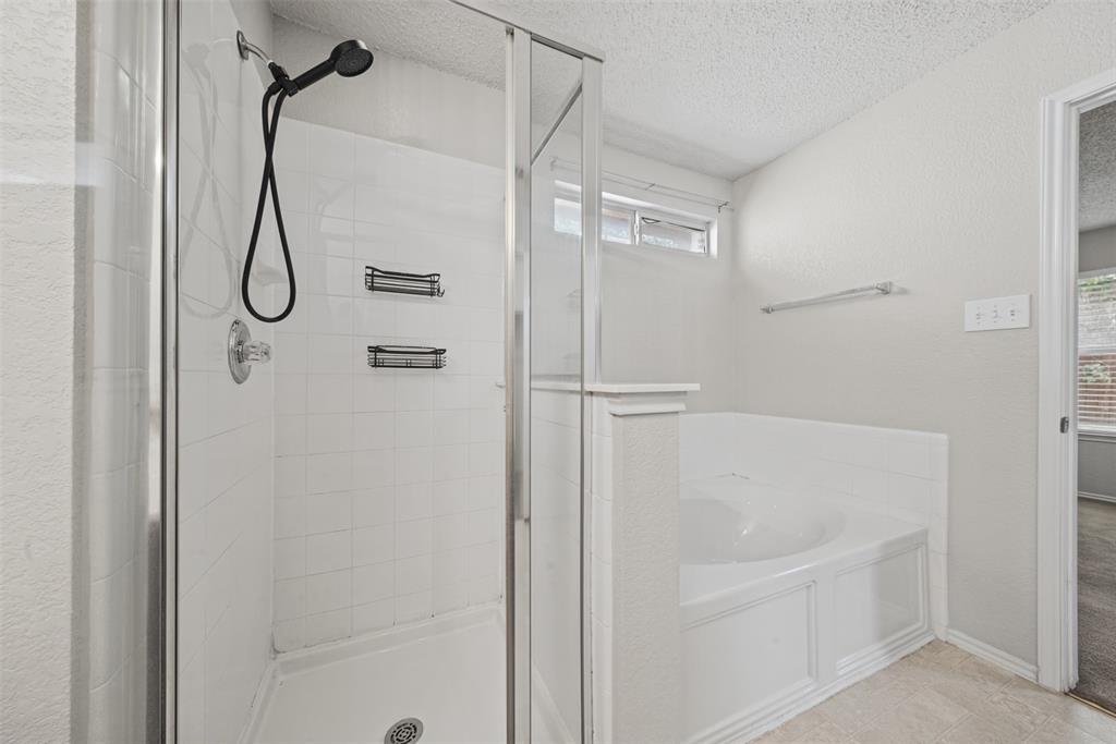 Walk-in shower with a glass enclosure, matte black rainfall shower head, white tile surround, built-in recessed shelving, and a separate soaking tub with a tiled apron front