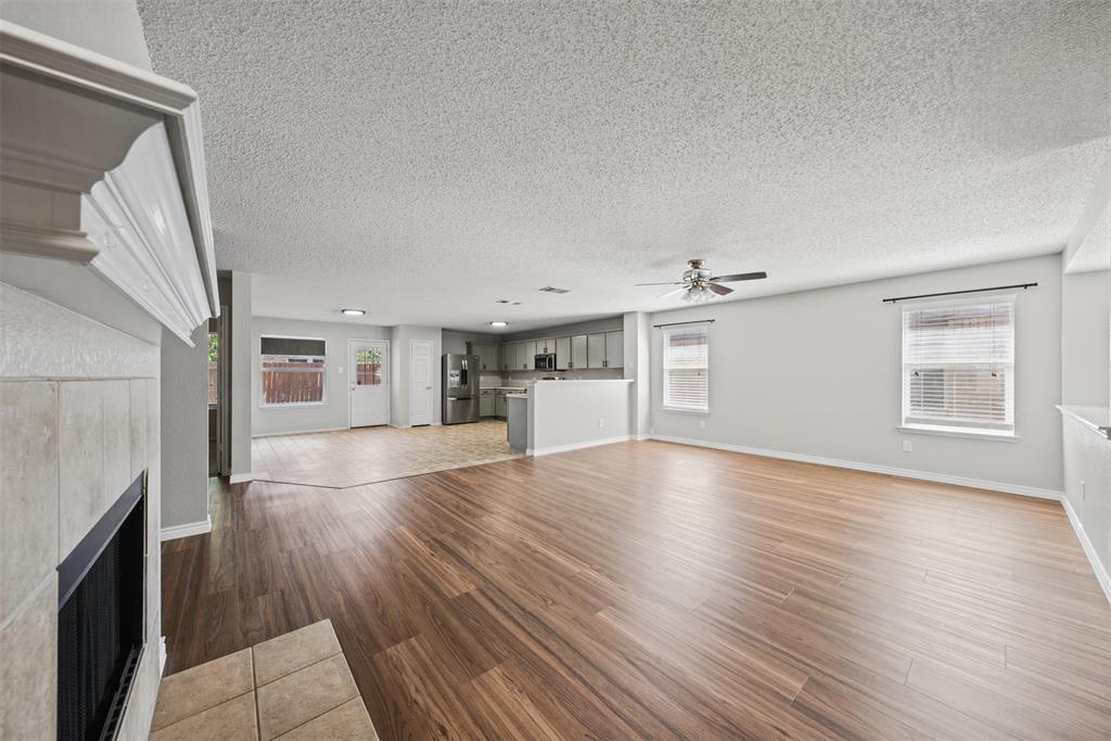Open-concept interior featuring wood-finish flooring, a tile-surround fireplace with a mantel, stainless steel kitchen appliances, and multiple windows