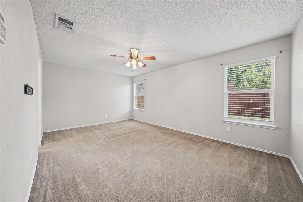 Neutral-toned interior room featuring wall-to-wall carpeting, a multi-blade ceiling fan with integrated lighting, and dual windows