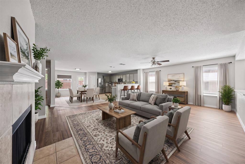 Open-concept floor plan featuring wood-finish flooring, a tile-surround fireplace with a mantel, and a kitchen island with built-in cabinetry