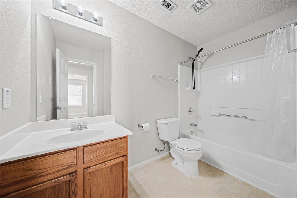 Bathroom featuring a vanity with wood-finish cabinetry, an integrated white sink, a full-length wall mirror, and a tub-shower combination with tile surround
