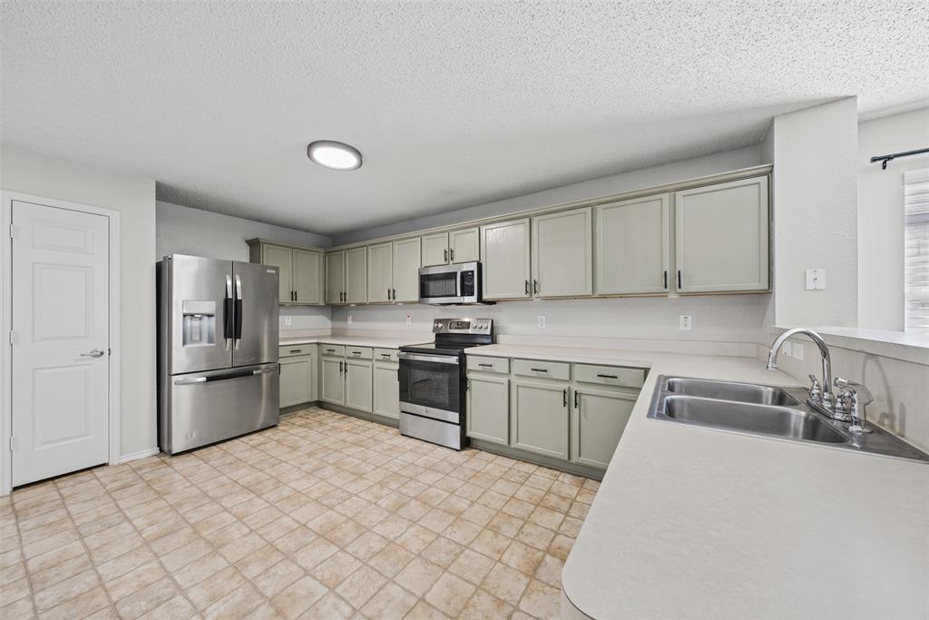 Kitchen featuring light-toned shaker-style cabinetry, stainless steel appliances, a dual-basin stainless steel sink, a flush-mount light fixture, and tile flooring