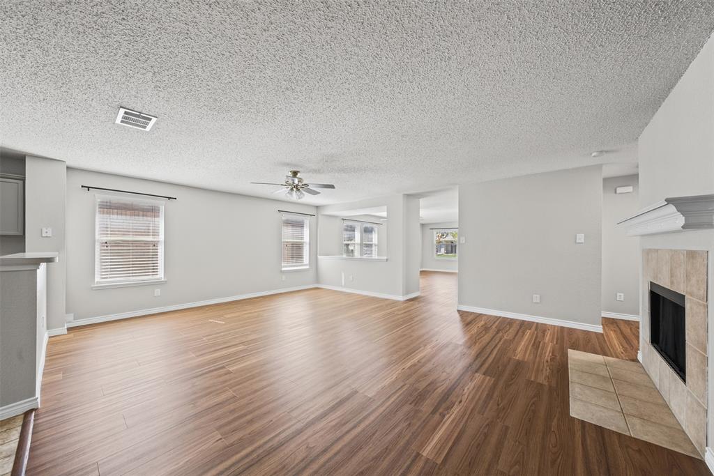 Open living area featuring wood-finish flooring, a fireplace with a stone-surround hearth, and a ceiling fan