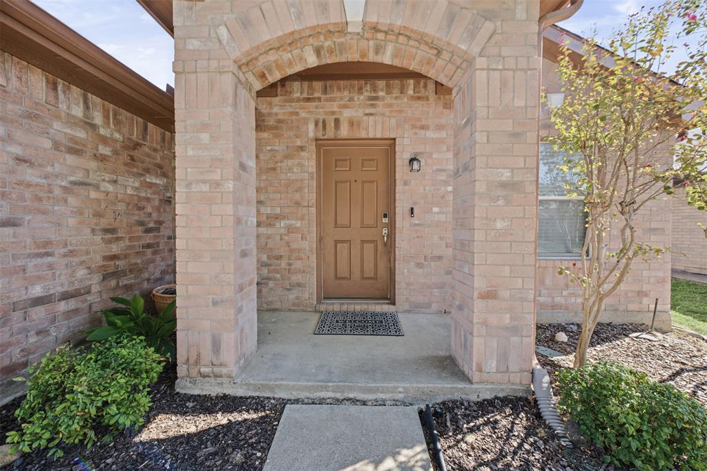 Brick exterior featuring a recessed front entryway, arched masonry detailing, a solid-panel door, and established landscaping Brick exterior featuring a recessed front entryway, arched masonry detailing, a solid-panel door, and established landscaping
