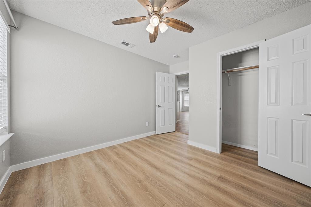 Room featuring wood-finish flooring, textured ceilings, a ceiling fan with integrated lighting, and a closet with a built-in hanging rod