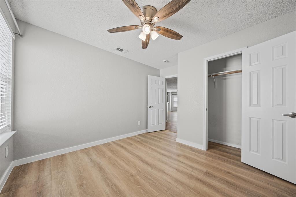 Neutral interior featuring wood-finish flooring, a multi-blade ceiling fan with integrated light fixture, and a reach-in closet with six-panel doors