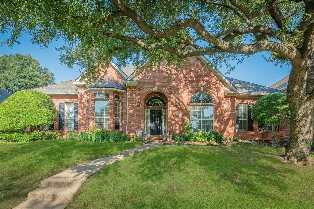 Brick exterior featuring a gabled roofline, arched window detailing, a covered entryway, and mature shade trees