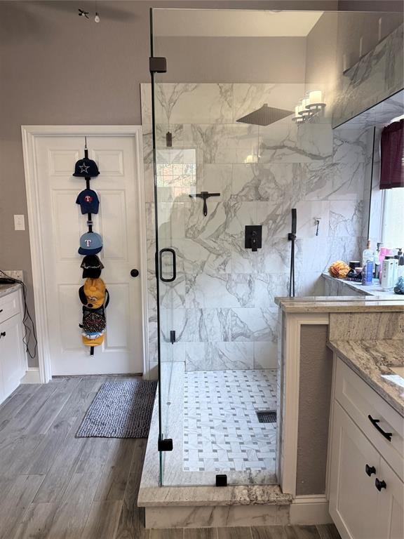 Walk-in shower featuring large-format patterned wall tile, a frameless glass enclosure, a rainfall showerhead, and a hand-held sprayer, complemented by white cabinetry and stone-finish countertops