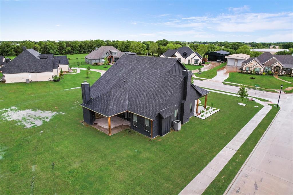 Aerial view of a residential property featuring an expansive lawn, concrete driveway, and multi-level roofline