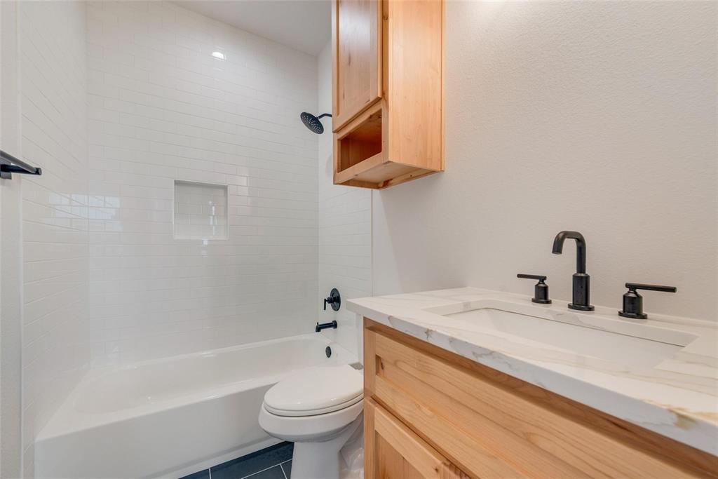 Bathroom featuring a wood-finish vanity with a stone-top integrated sink, matte black widespread faucet, subway tile shower surround with a built-in recessed niche, and matching wood-finish wall cabinetry