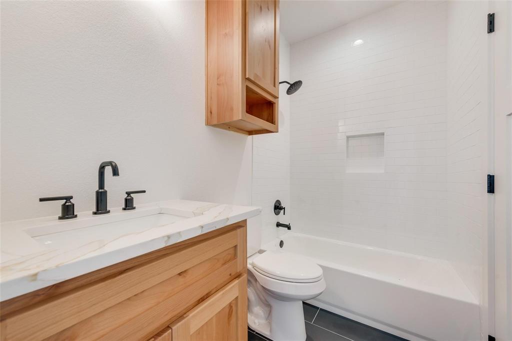 Natural wood vanity with stone-finish countertop, white subway tile shower surround with integrated niche, and matte black fixtures