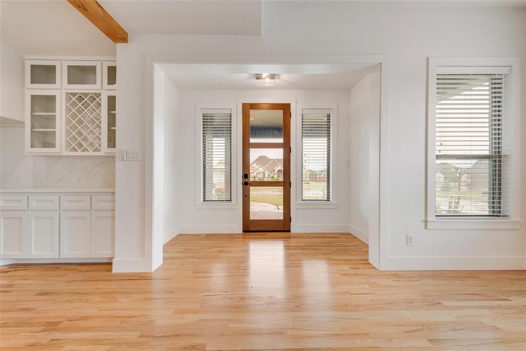 Wood-finish flooring, white cabinetry featuring built-in wine storage, and a natural wood-frame front door with glass panels