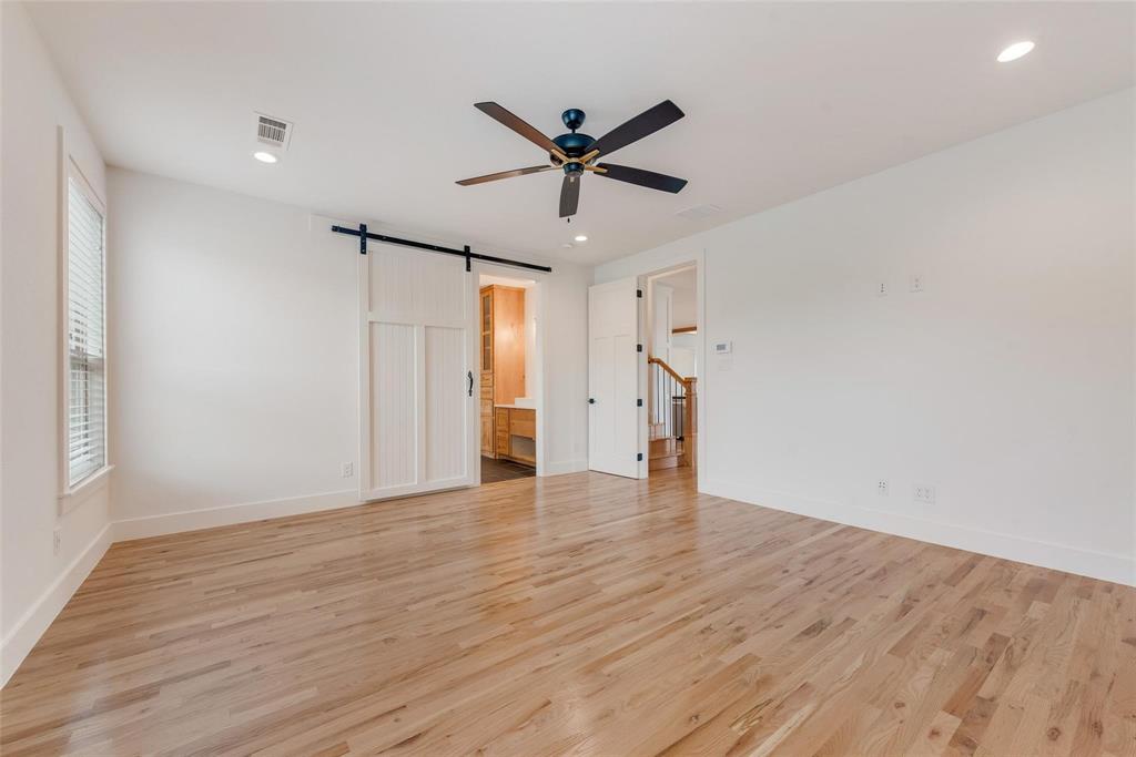 Room featuring wood-finish flooring, a white paneled sliding barn door, recessed lighting, and a dark-finish ceiling fan