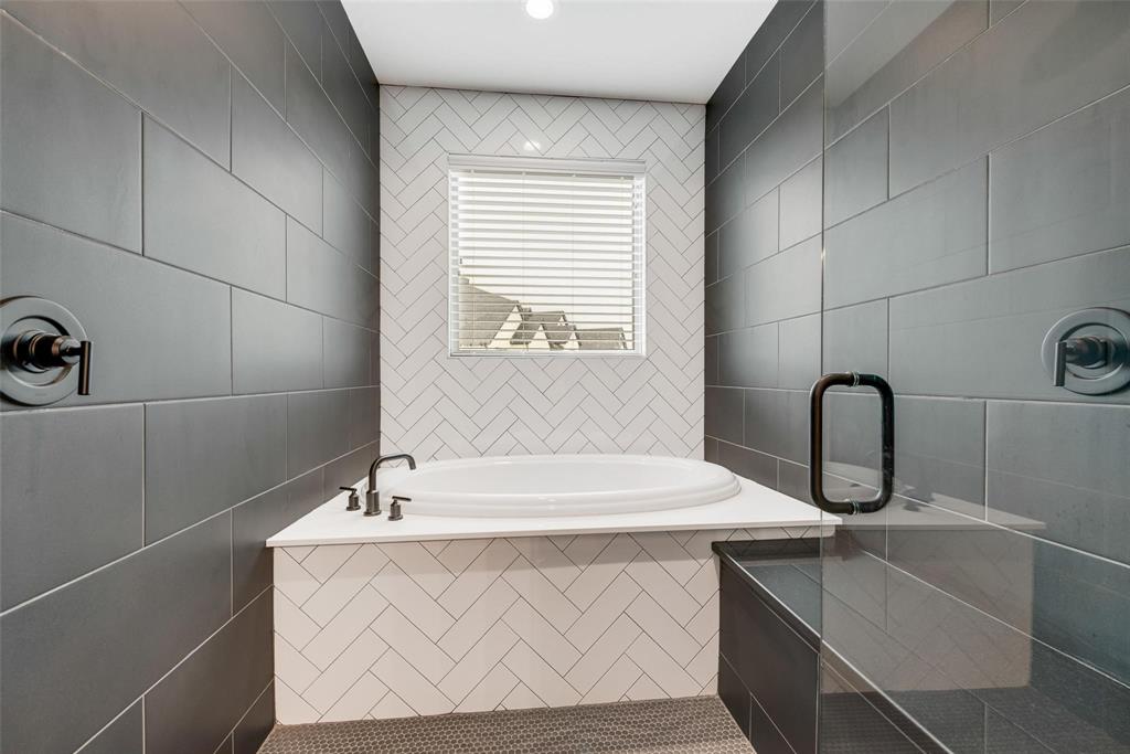 Deep soaking tub with a white surround and herringbone-patterned tile inlay, contrasting matte black plumbing fixtures, and large-format dark wall tile
