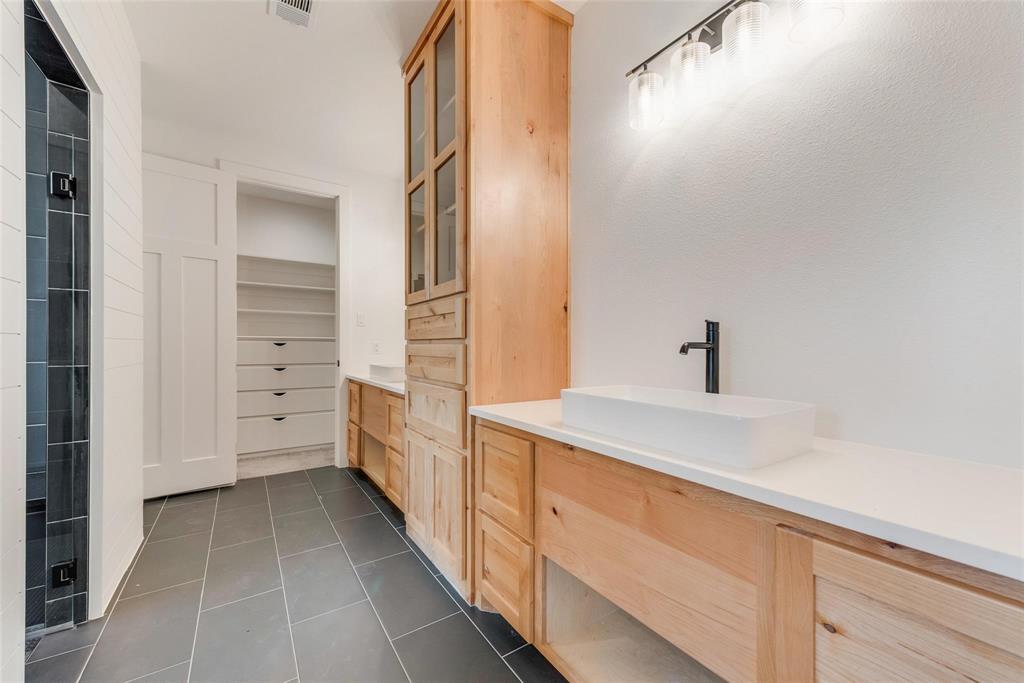 Custom wood cabinetry with an integrated tower, rectangular vessel sinks, light-toned solid surface countertops, matte black plumbing fixtures, and dark large-format tile flooring