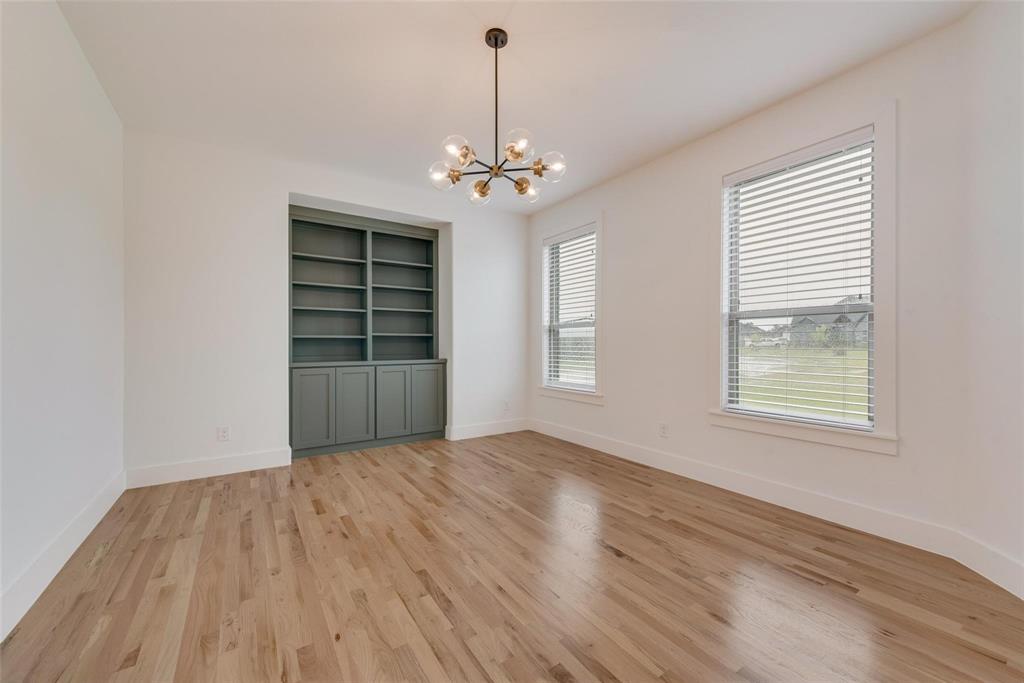 Room featuring wood-finish flooring, built-in floor-to-ceiling cabinetry, a multi-arm pendant light fixture, and two windows with horizontal blinds