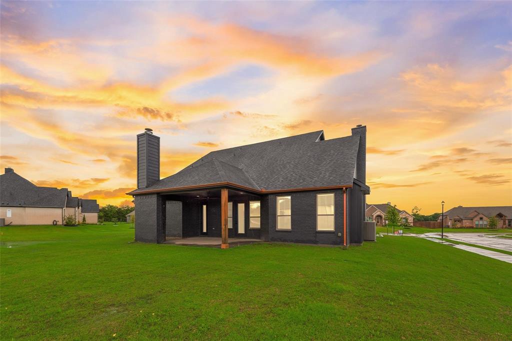 Dark exterior siding with a multi-gabled roofline, exterior brick chimneys, and a covered rear patio featuring wooden structural posts situated on a level lot