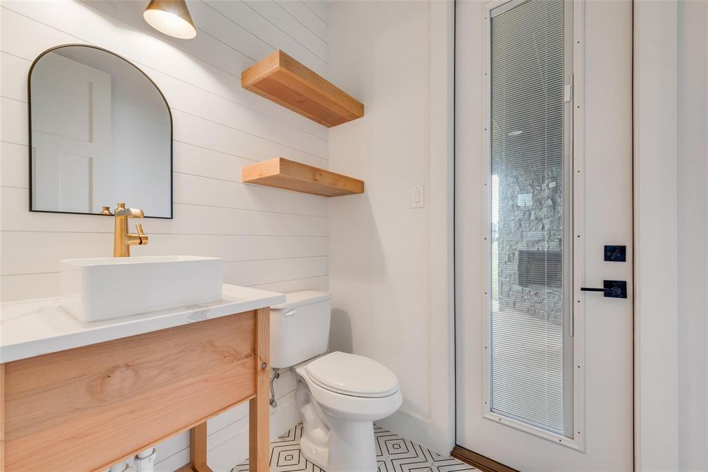 Custom wood-finish vanity with a white rectangular vessel sink, arched mirror, decorative shiplap wall detail, and geometric-patterned tile flooring