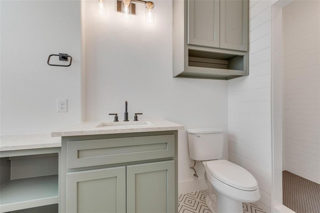 Shaker-style cabinetry, neutral-toned solid surface countertop, undermount sink with dark metallic hardware, wall-mounted cabinetry, and geometric patterned flooring