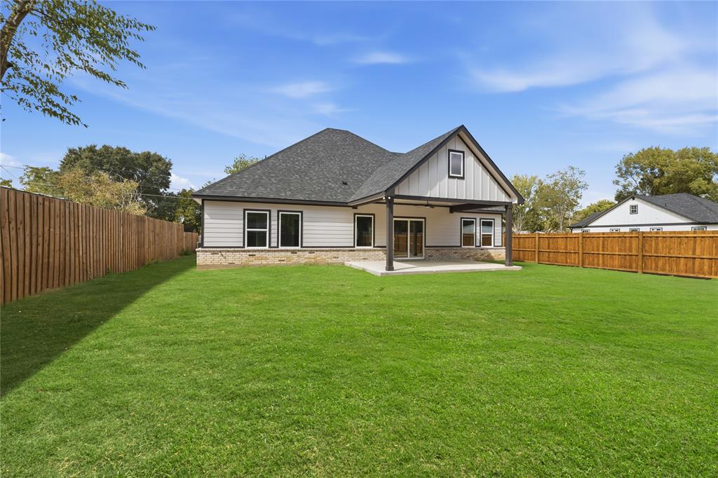 Rear exterior featuring a covered concrete patio, horizontal and vertical siding, stone masonry skirting, a gabled roofline, and a fenced backyard