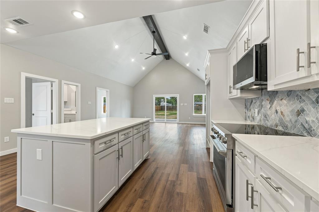 Kitchen featuring a vaulted ceiling with a decorative beam, central island with a quartz countertop, herringbone-patterned tile backsplash, stainless steel appliances, and wood-finish flooring