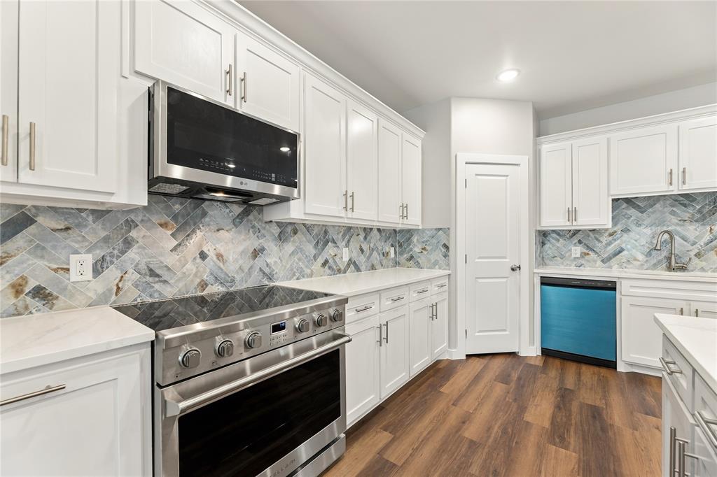 Kitchen featuring white Shaker-style cabinetry, herringbone-patterned stone tile backsplash, stainless steel range with overhead microwave, quartz countertops, and wood-finish flooring