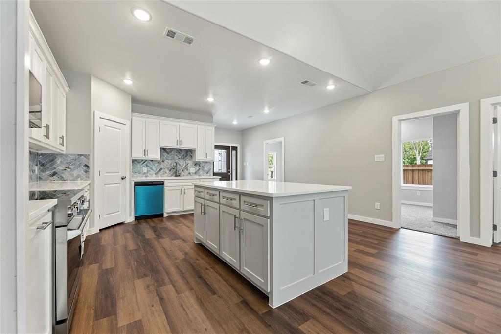 Kitchen featuring a central island with a solid surface countertop, white shaker-style cabinetry, a herringbone-patterned tile backsplash, stainless steel appliances, and wood-finish flooring