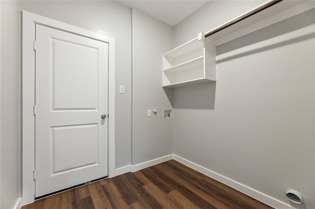 Utility area featuring wood-finish flooring, a solid-core interior door, wall-mounted white shelving, and a built-in hanging rod