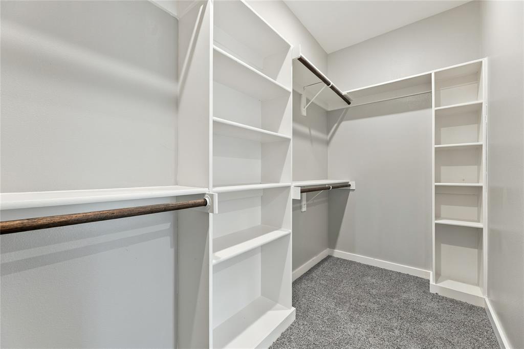 Walk-in closet featuring white built-in shelving, wooden garment rods, and wall-to-wall carpeting