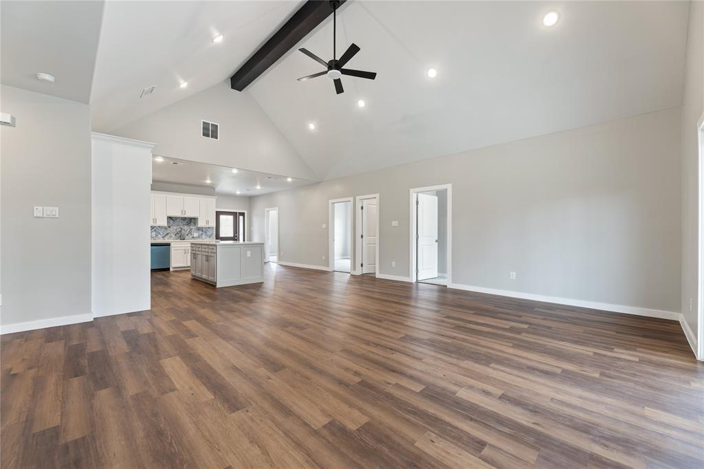 Open-concept interior featuring a vaulted ceiling, exposed structural beam, wood-finish flooring, recessed lighting, and a central kitchen island