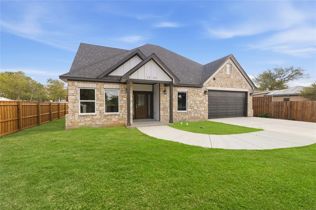 Single-story exterior featuring a stone facade, gabled roofline with peak detailing, dark-toned garage door, and covered entryway