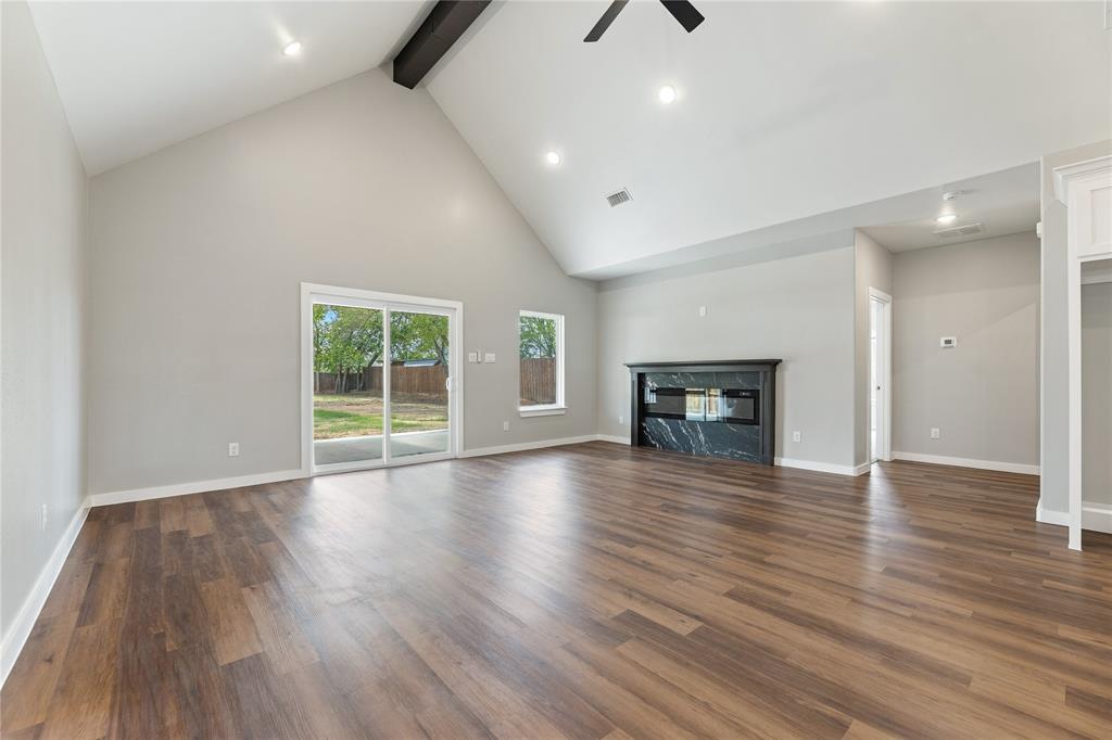 Vaulted ceiling with exposed beam, wood-finish flooring, fireplace with dark stone surround, and sliding glass door