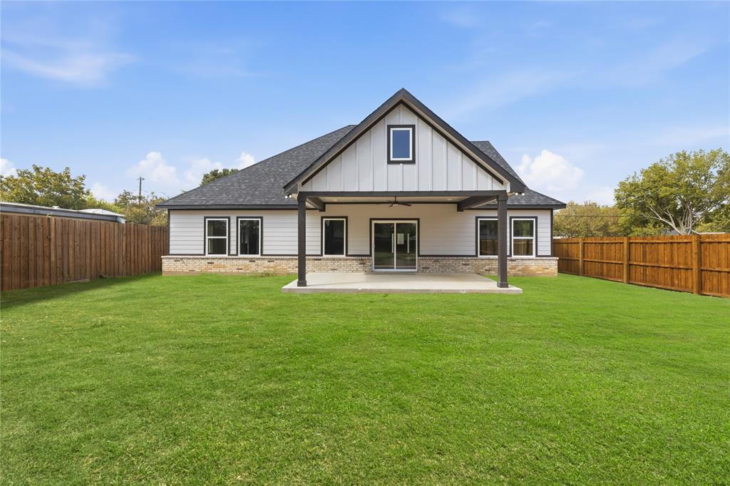 Exterior featuring a covered patio, vertical board-and-batten siding, stone masonry skirting, a gabled roofline, and wood-style privacy fencing