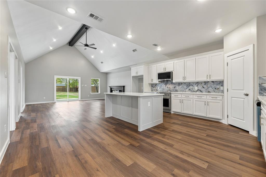 Vaulted ceilings, wood-finish flooring, central kitchen island with stone-finish countertop, herringbone-pattern tile backsplash, and recessed lighting