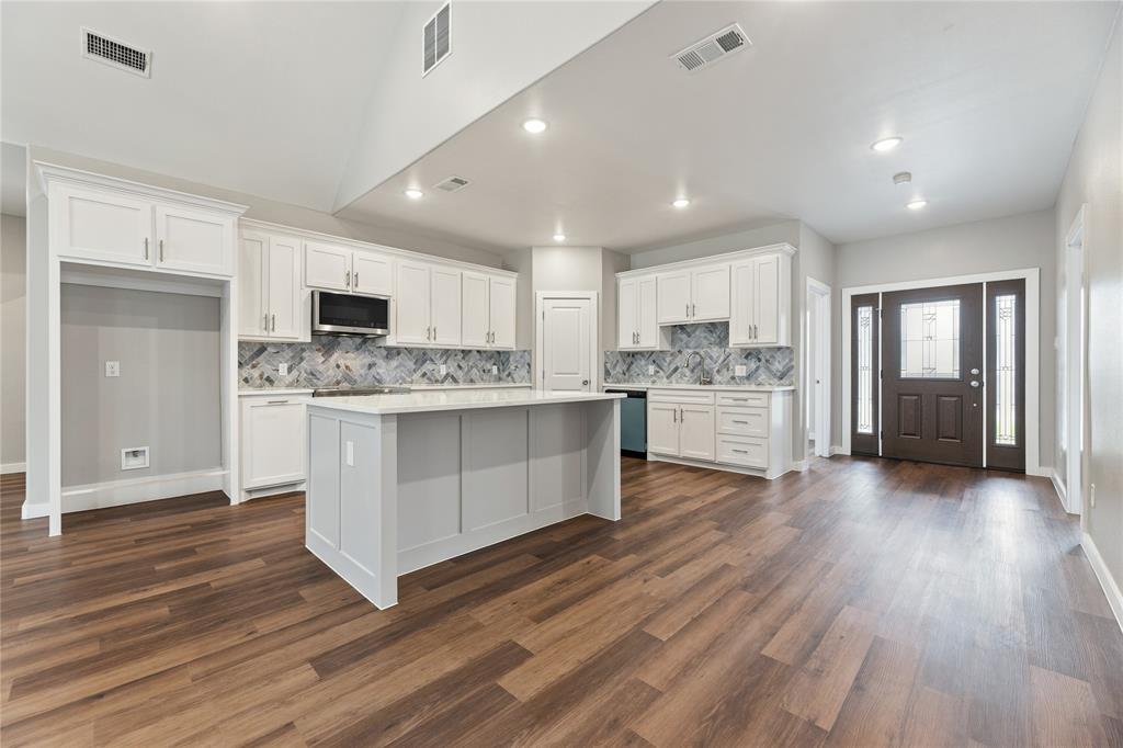 Kitchen featuring a vaulted ceiling, white cabinetry, a center island with solid surface countertops, herringbone pattern tile backsplash, and wood-finish flooring