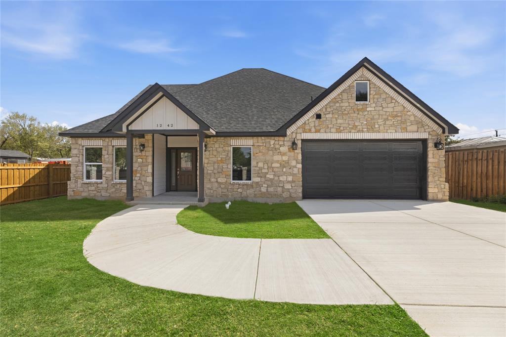 Stone veneer exterior with dark-finish gabled roof, concrete driveway, two-car garage, and wood-toned privacy fencing