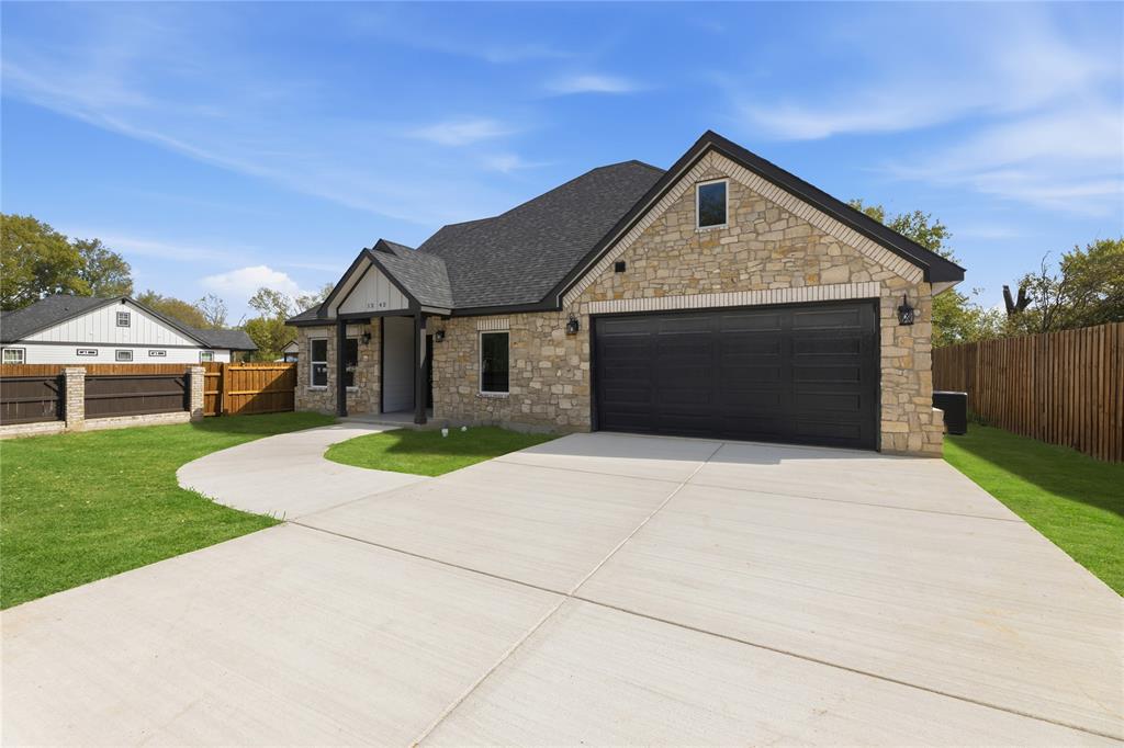 Stone masonry exterior with a multi-gabled asphalt shingle roof, two-car garage with dark-finish door, and concrete driveway