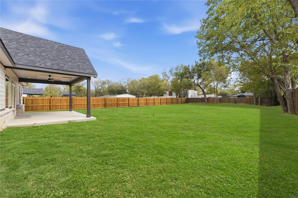 Expansive backyard featuring a covered patio, concrete flooring, a ceiling fan, and perimeter wood fencing