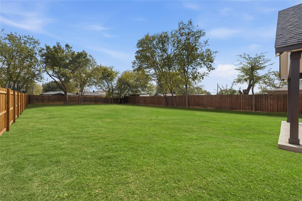 Expansive backyard featuring a large grass lawn, perimeter wood fencing, and mature trees