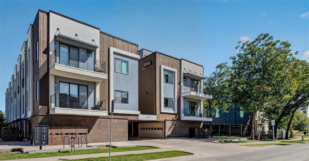 Contemporary multi-story exterior featuring a mix of stucco and wood-finish siding, recessed covered parking, private balconies with metal railings, and prominent masonry detailing Contemporary multi-story exterior featuring a mix of stucco and wood-finish siding, recessed covered parking, private balconies with metal railings, and prominent masonry detailing