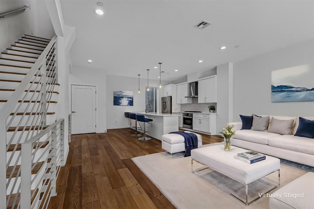 Open-concept interior featuring wood-finish flooring, a kitchen island with pendant lighting, shaker-style cabinetry, and a stainless steel range hood