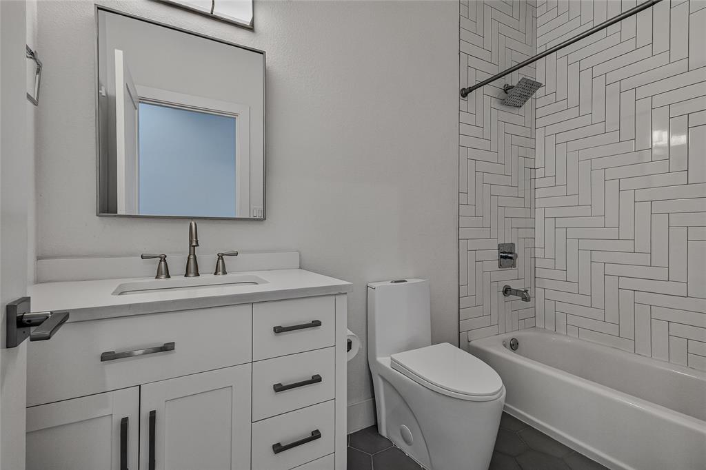 Bathroom featuring a white vanity with a composite countertop, rectangular undermount sink, herringbone tile shower surround, and dark hexagonal floor tile