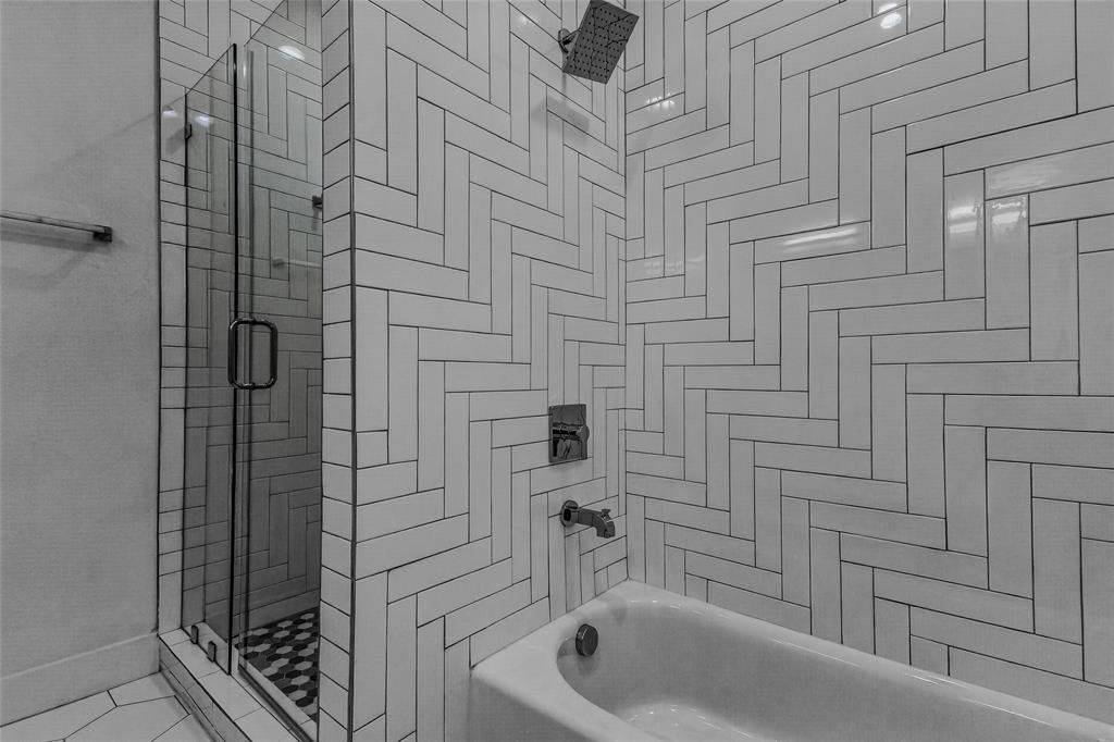 Shower and bathtub combination featuring white rectangular wall tile in a herringbone pattern, a glass shower enclosure, a rainfall showerhead, and metallic fixtures