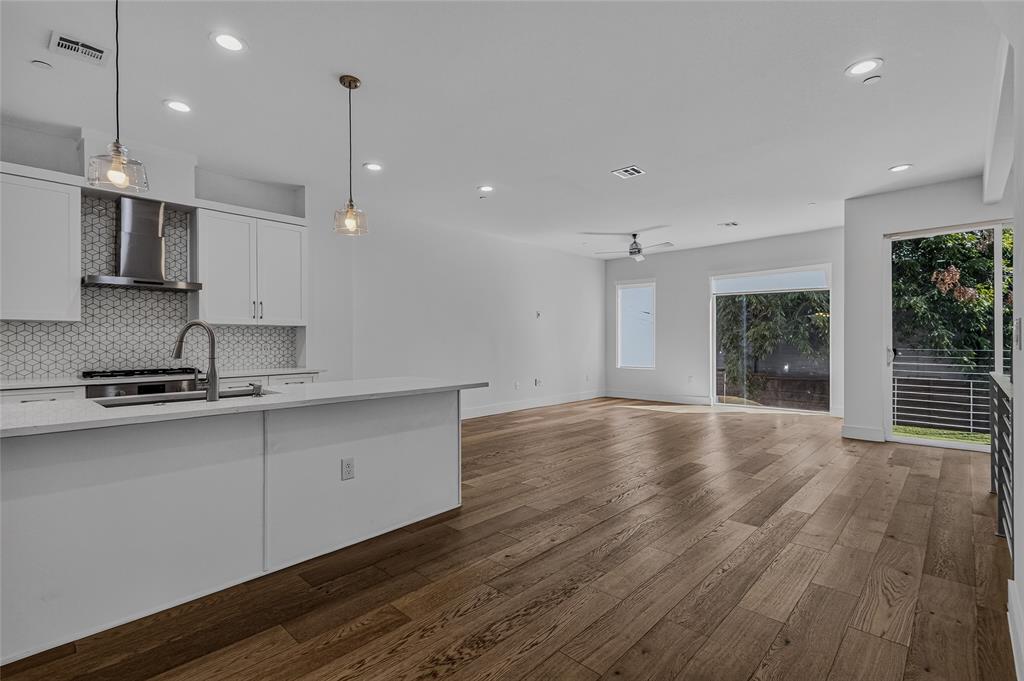 Open-concept kitchen featuring a stone-topped island, geometric patterned tile backsplash, stainless steel range hood, recessed ceiling lighting, and wide-plank wood-finish flooring