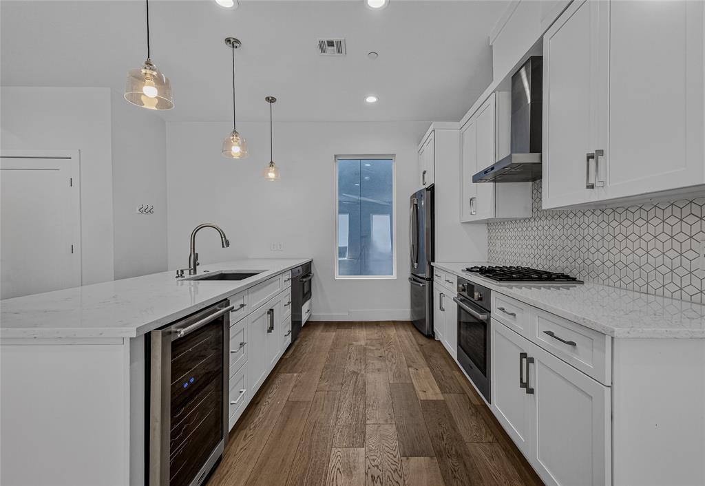 Kitchen featuring white cabinetry, quartz countertops, geometric tile backsplash, stainless steel appliances including a built-in wine cooler, and wood-finish flooring