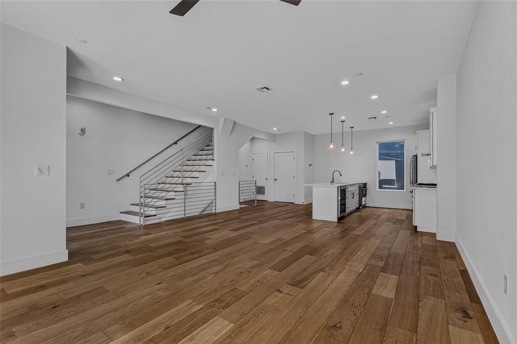 Open-concept interior featuring wood-finish flooring, recessed lighting, a center kitchen island with a sink, and a staircase with metal horizontal railings